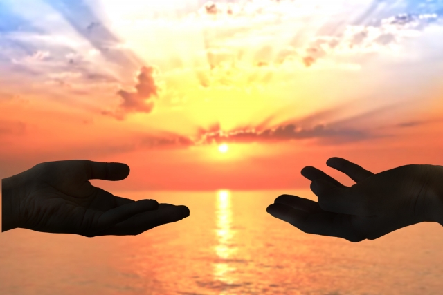 夕日を獏に手を差し出している影のシルエット